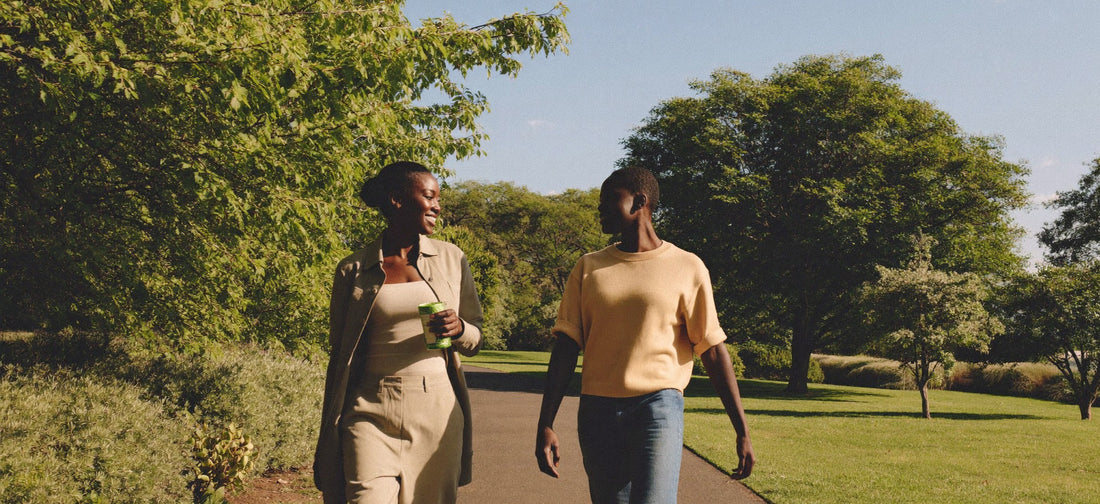 Two young Black South African adults sharing a light moment after a walk in a leafy urban park, photographed naturally in warm afternoon light.