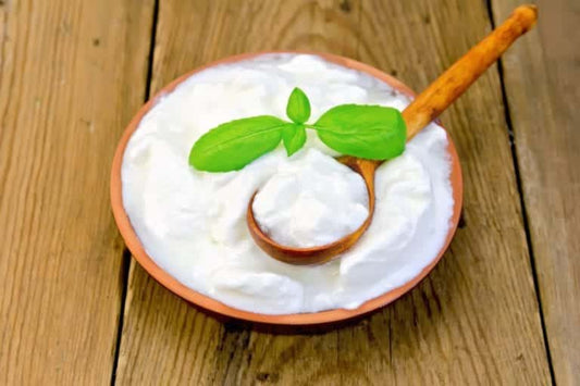 Bowl of creamy yogurt with wooden spoon and basil leaves on wooden surface, illustrating probiotics for health benefits.
