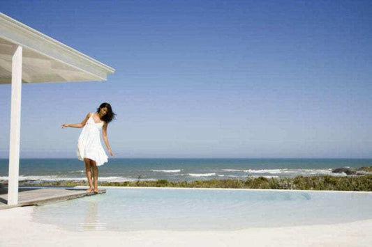 woman in white dress balancing near clear pool with ocean background
