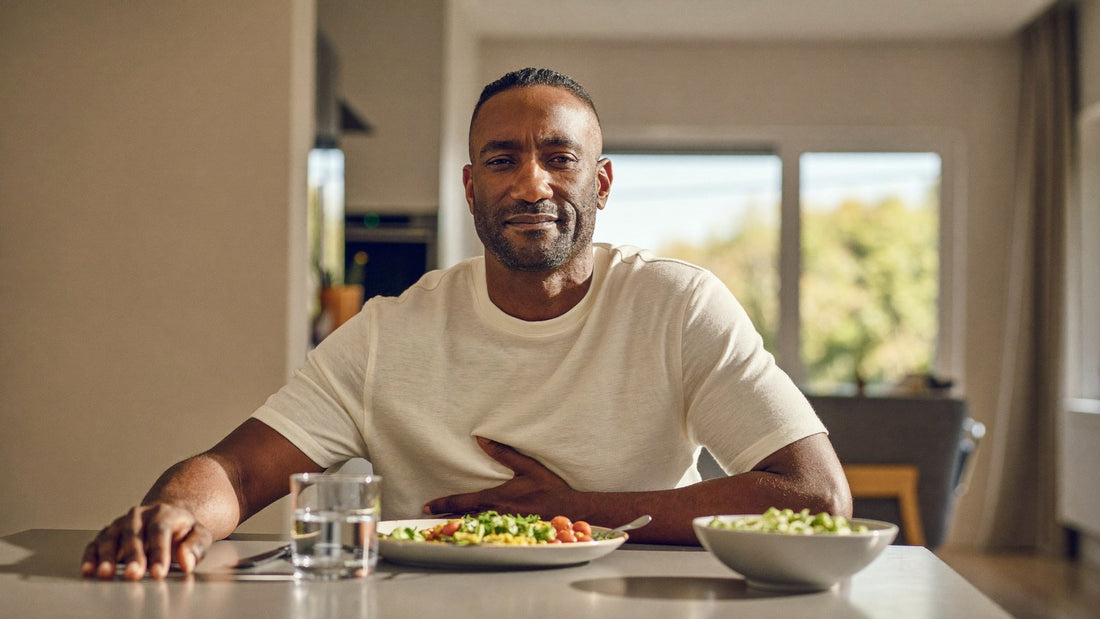 Man resting his hand on his stomach after a meal at a sunlit kitchen table