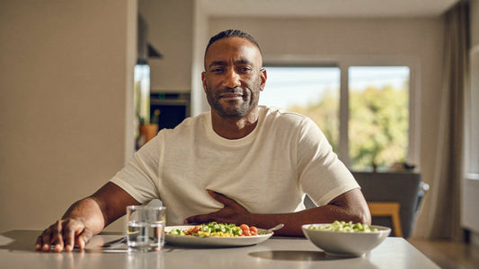 Man resting his hand on his stomach after a meal at a sunlit kitchen table