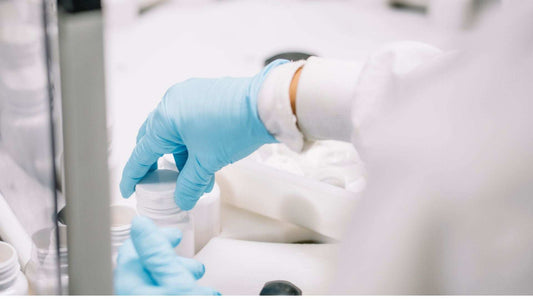 scientist in blue gloves handling white pharmaceutical containers for encapsulation of sensitive actives in a lab