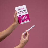 Hands holding Femina Suppository Applicators box and a single applicator against pink background