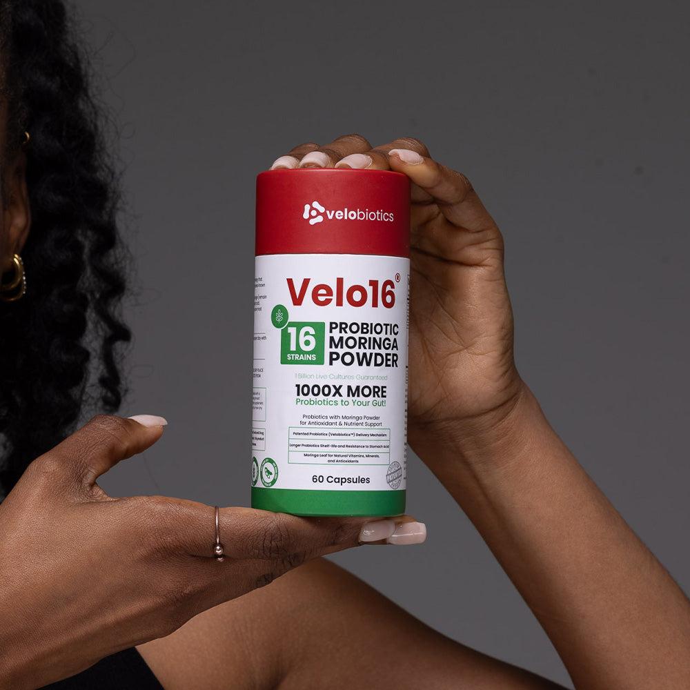 Velo16 Probiotics Moringa Powder supplement bottle held by hands on gray background